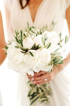 a bride holding a bouquet of white peonies and greenery on her wedding day