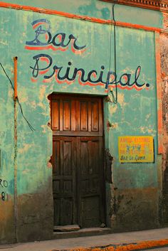 an old building with graffiti on it's side and a wooden door that says bar principal