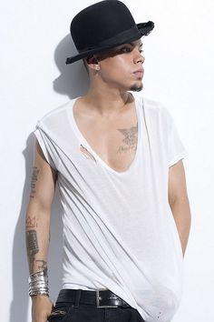 a man with tattoos wearing a white shirt and black hat standing next to a wall