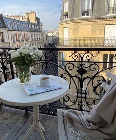 a table with flowers and a book on it next to a balcony overlooking the city