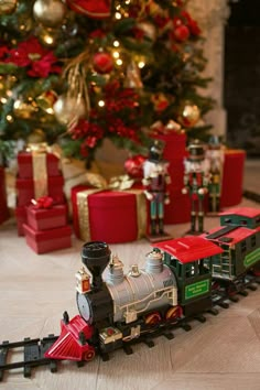 a toy train is on the tracks in front of a christmas tree with presents around it