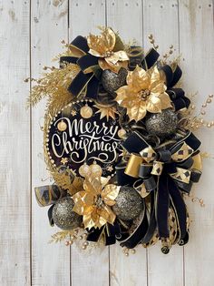 a black and gold wreath with merry christmas written on it sitting on a wooden surface