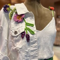 a white shirt with crocheted flowers on the front and green shorts underneath it