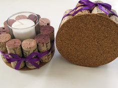 a candle and some corks with purple ribbon around them on a white table top