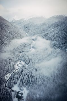 an aerial view of the mountains and trees covered in snow, with a river running between them