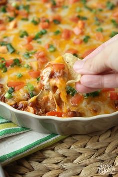 a person scooping some food out of a casserole dish with cheese and veggies