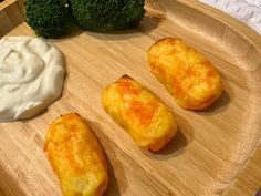 three pieces of bread on a wooden tray with some dip and broccoli in the background