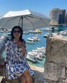 a woman sitting under an umbrella on the side of a stone wall next to boats