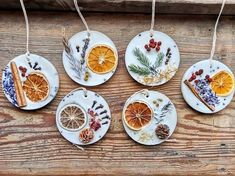 four ceramic ornaments with dried orange slices and spices hanging from strings on a wooden surface