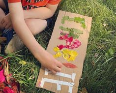 a young boy sitting in the grass with flowers on a piece of cardboard taped to it