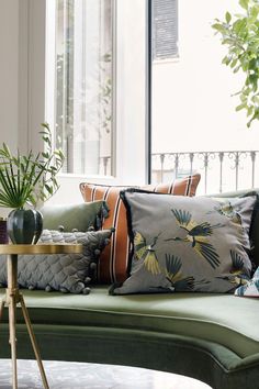 a green couch with pillows and plants on it in front of a large glass window