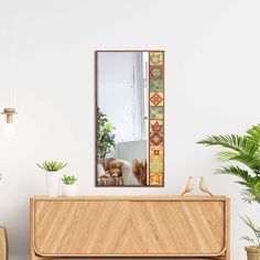 a mirror sitting on top of a wooden dresser next to a potted palm tree