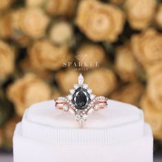 a black diamond ring sitting on top of a white display stand with roses in the background