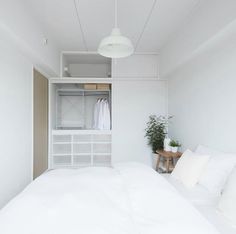 a white bed sitting in a bedroom next to a shelf filled with pillows and blankets