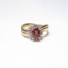 a gold ring with a red stone surrounded by small white and pink diamonds on the band