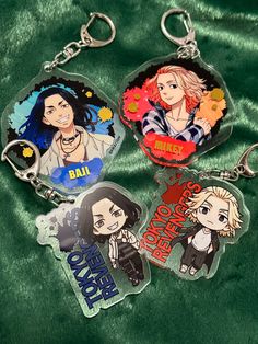 three keychains with anime characters on them sitting on a green cloth covered surface