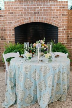 a table is set up with flowers and candles for a wedding reception in front of a brick fireplace