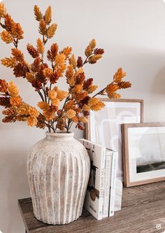 a white vase filled with orange flowers sitting on top of a wooden shelf next to pictures