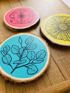 three wood slices with flowers painted on them sitting on a wooden table next to each other