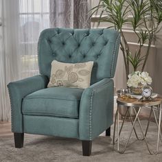 a blue chair sitting in front of a window next to a table with a clock on it