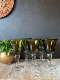 four wine glasses sitting on top of a wooden table next to a potted plant