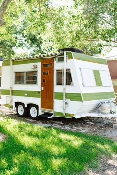 an rv is parked under a tree on the grass in front of a house with green trim