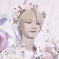 a man with flowers in his hair and a flower crown on his head, standing next to a wall