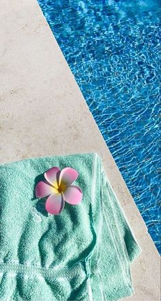 a towel and flower sitting on the edge of a swimming pool next to a blue water