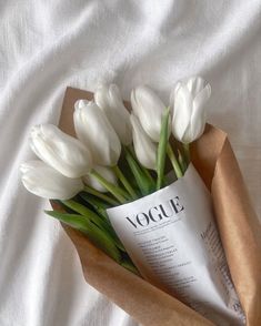 a bouquet of white tulips is wrapped in brown paper and sits on a bed