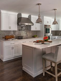 a large kitchen with white cabinets and an island in the middle is surrounded by two gray bar stools