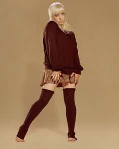 a woman with blonde hair wearing tights and stockings, standing in front of a brown background