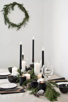 the table is set with black and white dishes, candles, pine cones, and evergreen garland