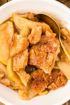 a white bowl filled with apple cobbler next to a yellow spoon on top of a wooden table