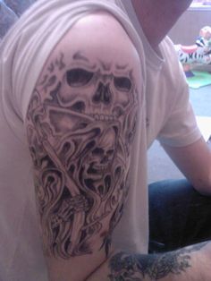 a man with a skull tattoo on his arm and shoulder is sitting in front of the camera