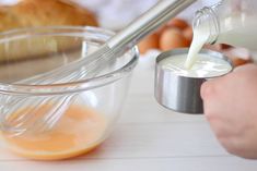 someone pouring milk into a glass bowl with an orange in it and croissants on the side