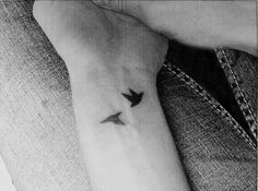 a black and white photo of a person's arm with a small bird tattoo on it