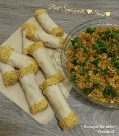 some food is in a glass bowl and on a napkin next to it are rice rolls