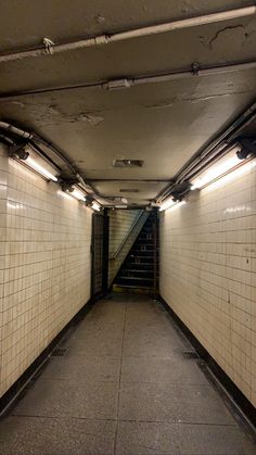 an empty subway tunnel with stairs leading up to the second floor and tiled walls on either side