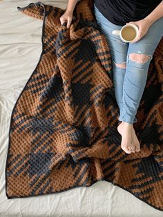 a woman sitting on top of a bed next to a blanket holding a cup of coffee