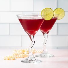 two glasses filled with red liquid and garnished with lime