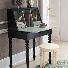 a black desk with two drawers and a small stool in front of it on a rug