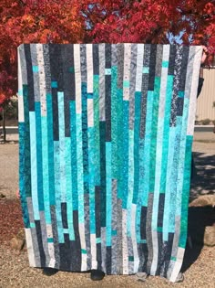 a blue and black quilt sitting on top of a stone slab next to a tree