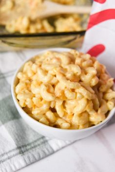 macaroni and cheese in a white bowl on a checkered tablecloth next to a glass dish