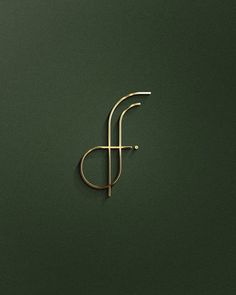 the letter f is made out of gold wire and sits on a dark green surface