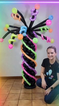 a woman kneeling down next to a fake tree with balloons on it's branches