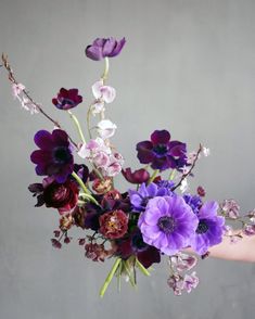 a woman holding a bouquet of flowers in her hand with purple and white blooms on it