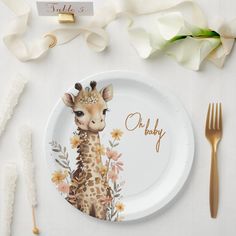 a white plate with a giraffe on it next to flowers and goldware