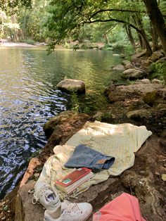 an open book and some books on a blanket by the water with trees in the background