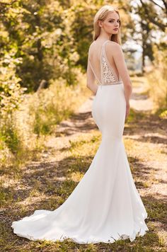 a woman in a white wedding dress standing on a dirt road with trees and grass behind her