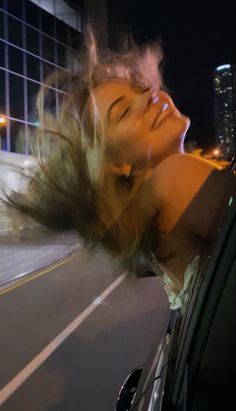 a woman leaning out the window of a car on a city street at night with her hair blowing in the wind